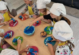 Dzieci dekorują niebieskim kremem babeczki